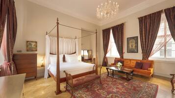 A four-poster bed with a canopy, a wooden bench, a sofa, a coffee table, and a chandelier.