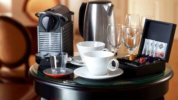 Eine Kaffeemaschine, ein Wasserkocher, zwei Tassen, zwei Gläser und eine Teeaufbewahrungsbox auf einem Glastisch.