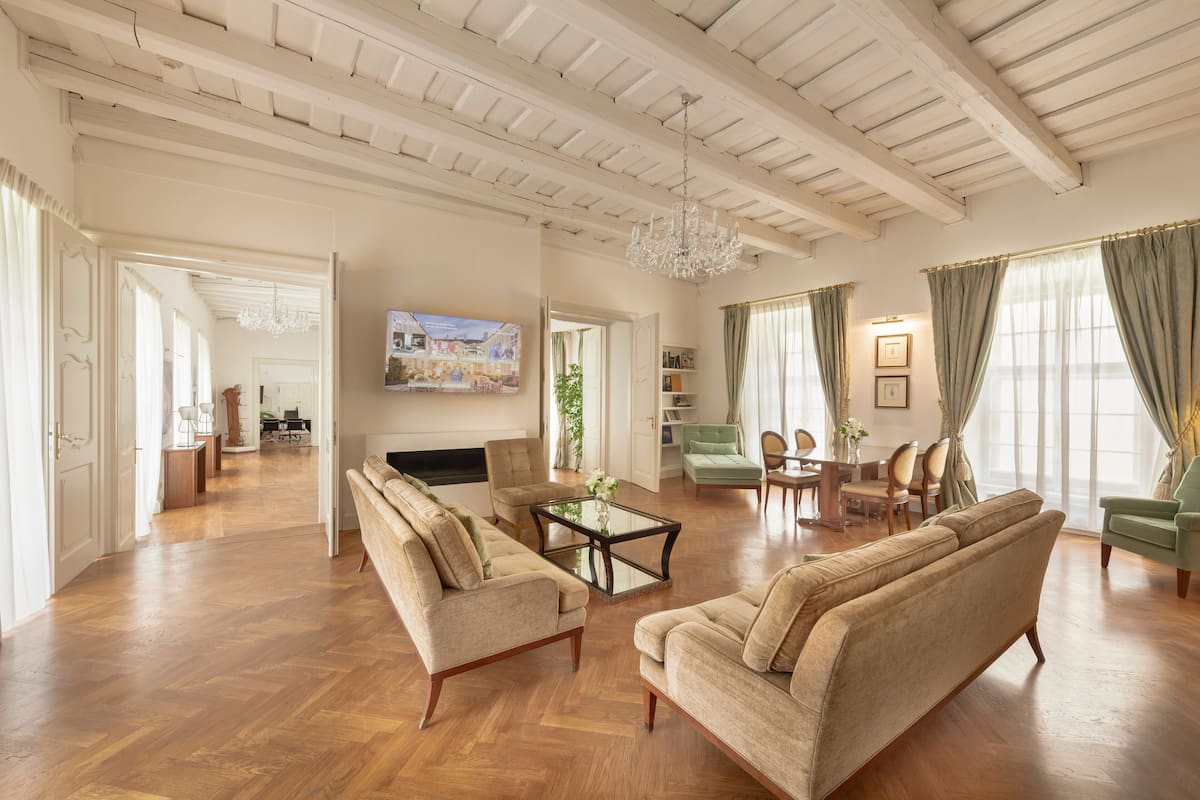 A spacious living room with wooden flooring, a large sofa, a coffee table, and a chandelier.