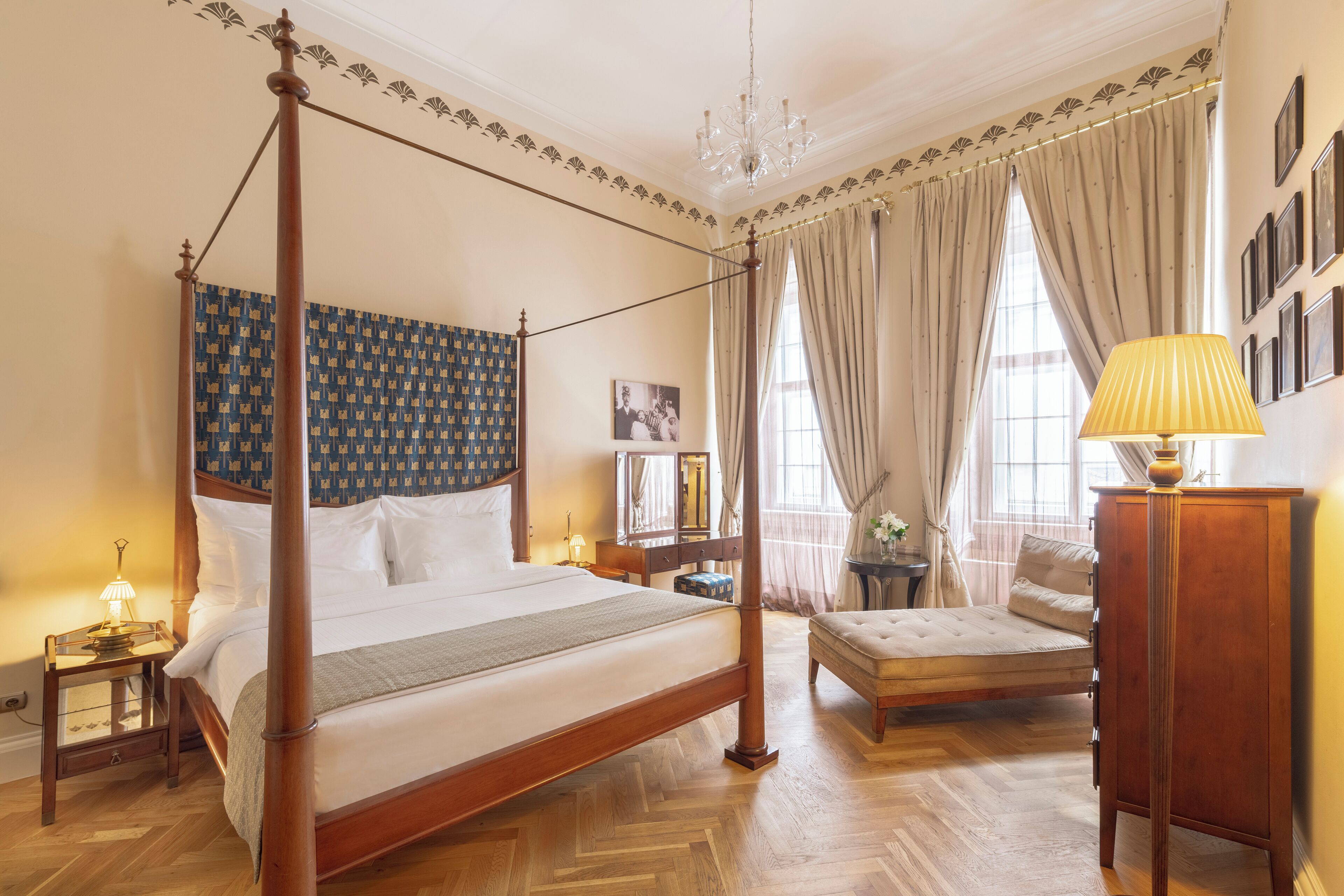 A four-poster bed with a wooden headboard, a bedside table with a lamp, a bench, and a wooden cabinet.