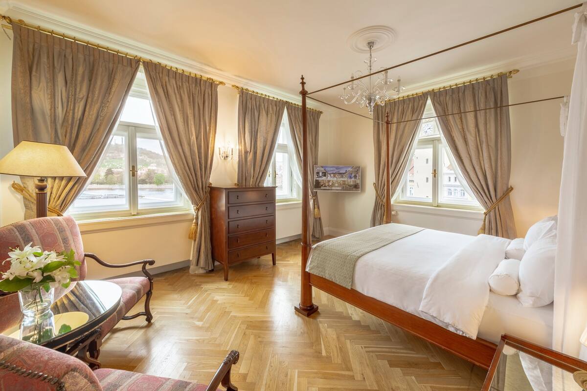 A bedroom with a four-poster bed, a dresser, a chair, and a table with a lamp.