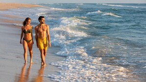 Une scène de plage où l’on voit deux personnes se promenant le long du rivage.