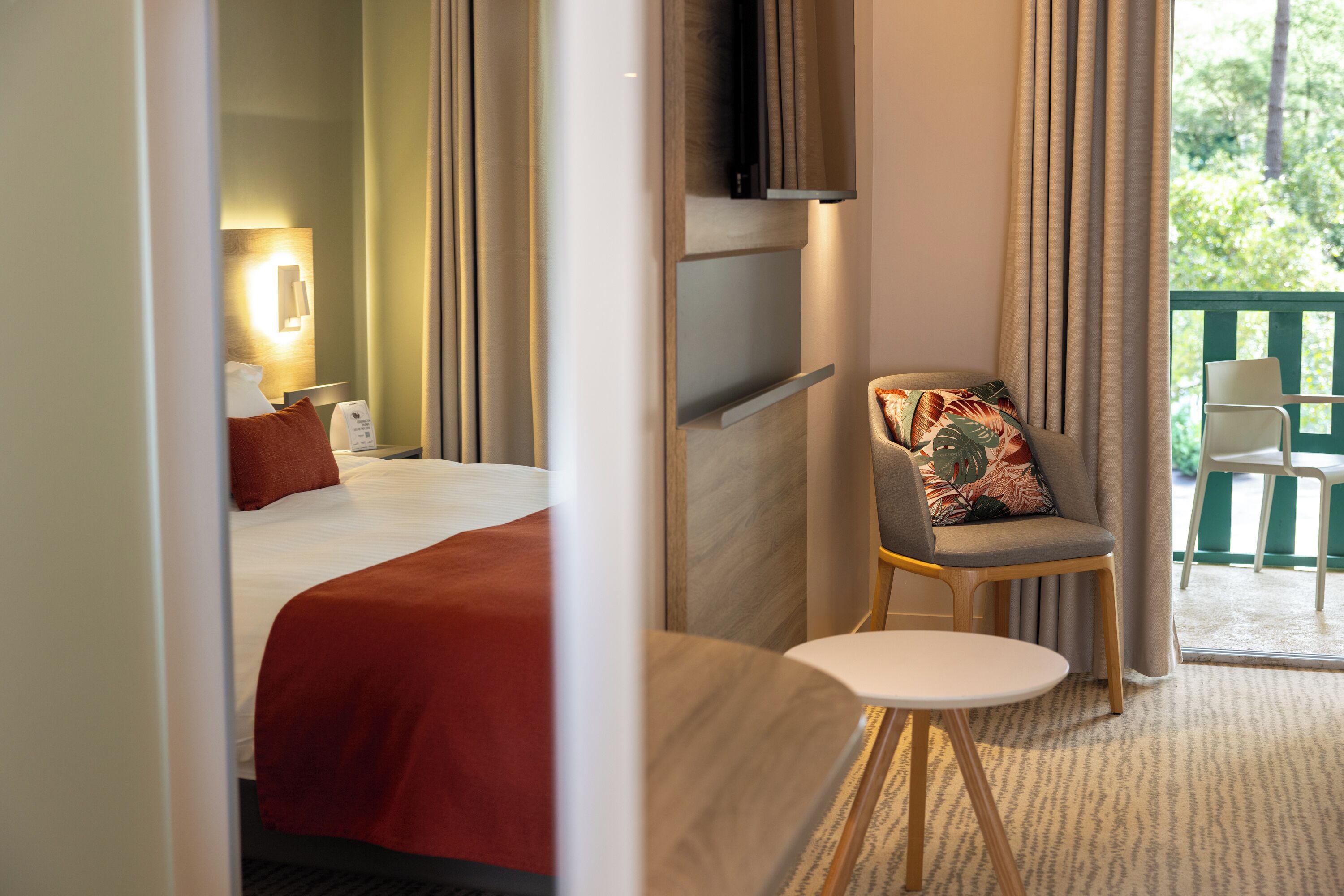 A hotel room with a bed, a chair, a small table, and a TV mounted on the wall.
