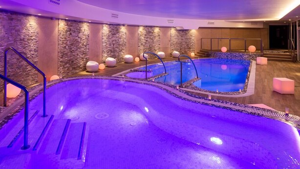 Un espace de bien-être doté d’une grande piscine intérieure, de murs en pierre et d’un éclairage moderne.