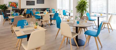 A modern dining area with round tables and blue chairs, featuring a large plant and a colorful painting on the wall.