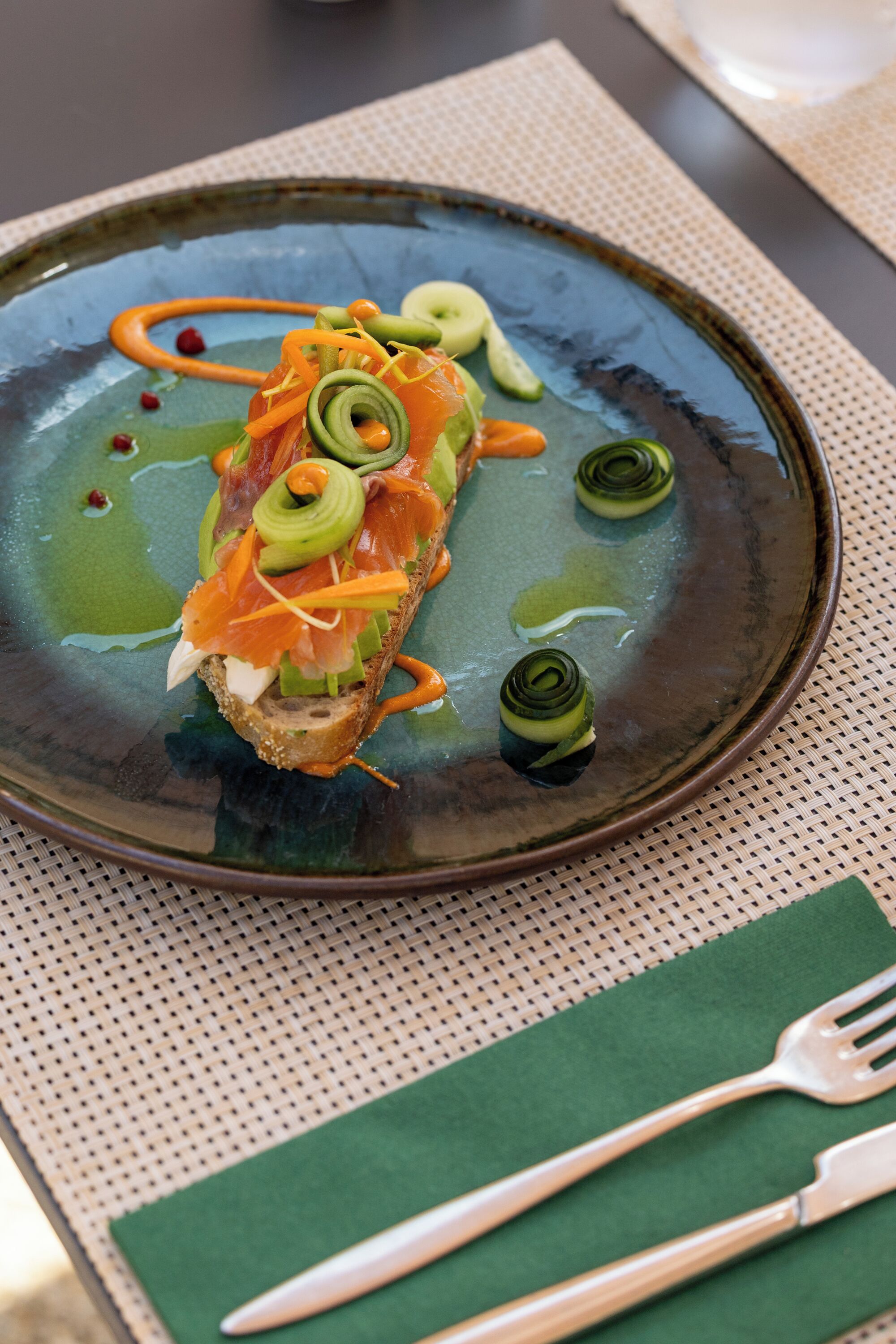 A plate with a sandwich, green sauce, and a fork on a table.