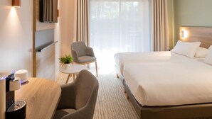 Une chambre d’hôtel comprenant un lit, un bureau avec une chaise, un téléviseur fixé au mur et une petite table avec une plante.