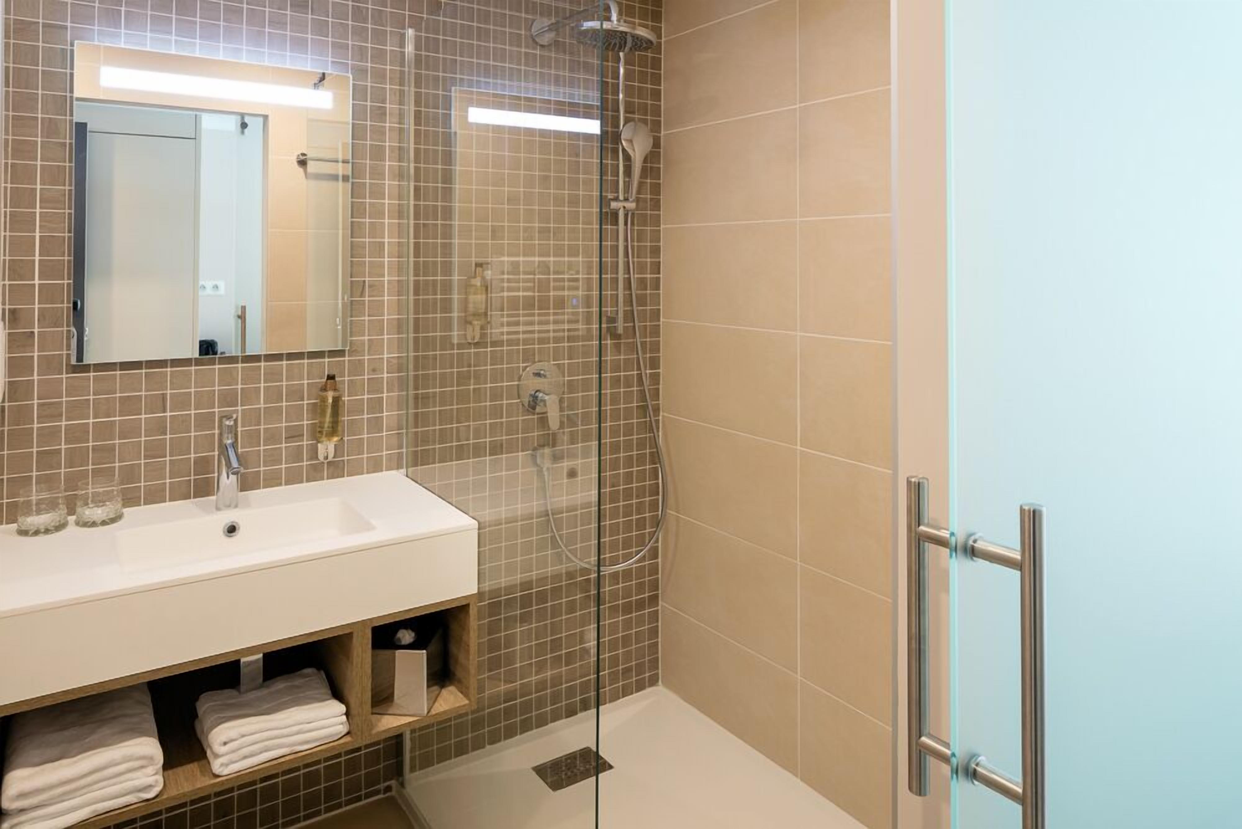 A modern bathroom with a glass-enclosed shower, a white sink, and a mirror above it.