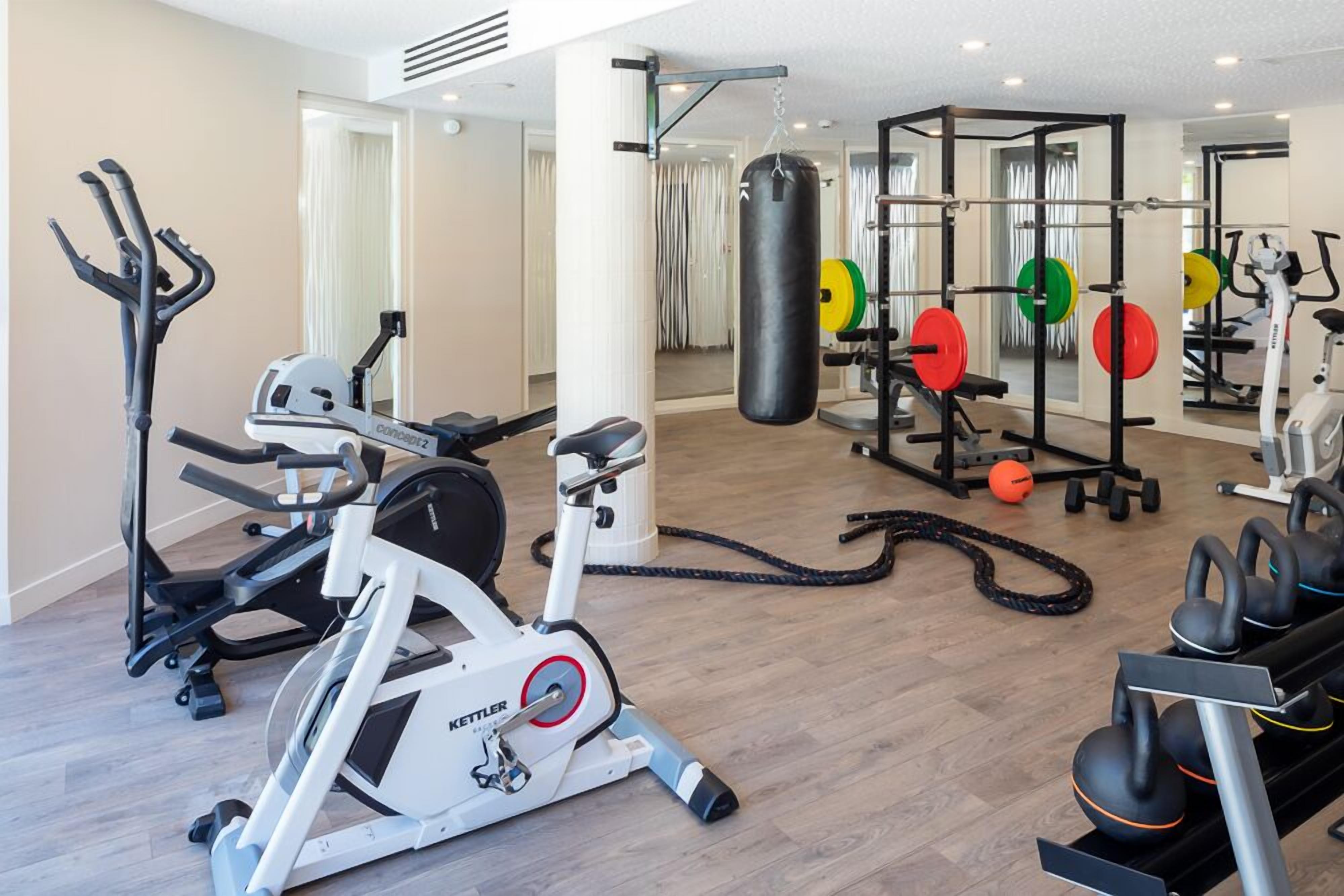 Une salle de sport équipée de machines de cardio, de postes d’entraînement en musculation et d’un sac de frappe.
