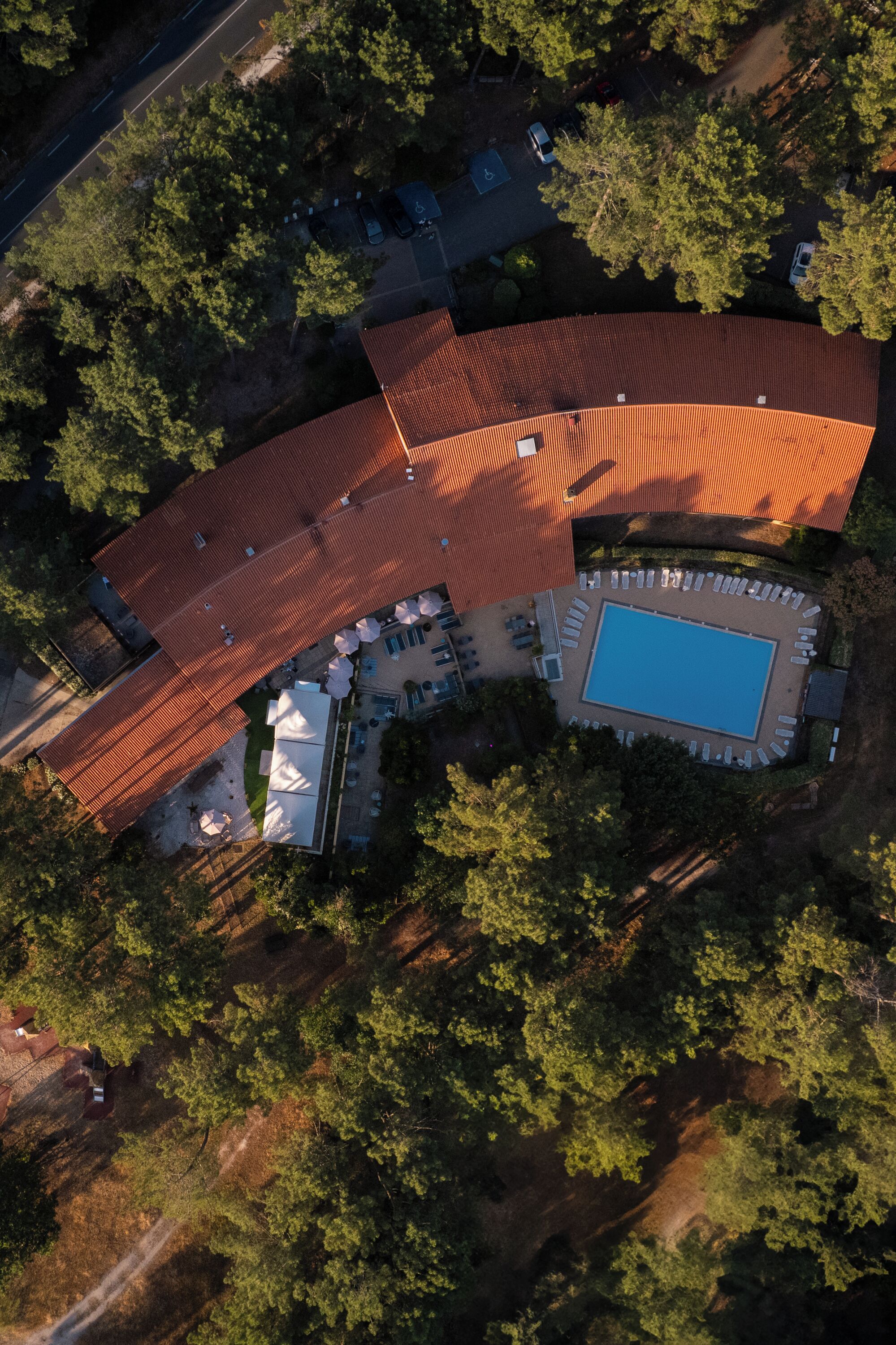 An aerial view of a property with a swimming pool, outdoor seating, and a large building with a red roof.