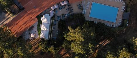 An aerial view of a property with a swimming pool, outdoor seating, and a large building with a red roof.