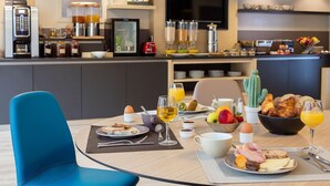 Un coin petit-déjeuner moderne, comprenant une table à manger, des chaises et une variété d’aliments pour le petit-déjeuner, notamment des œufs, des toasts, des fruits et des boissons.