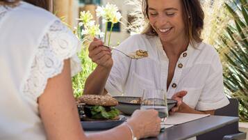 Two people dining outdoors at a table with a meal, surrounded by greenery.