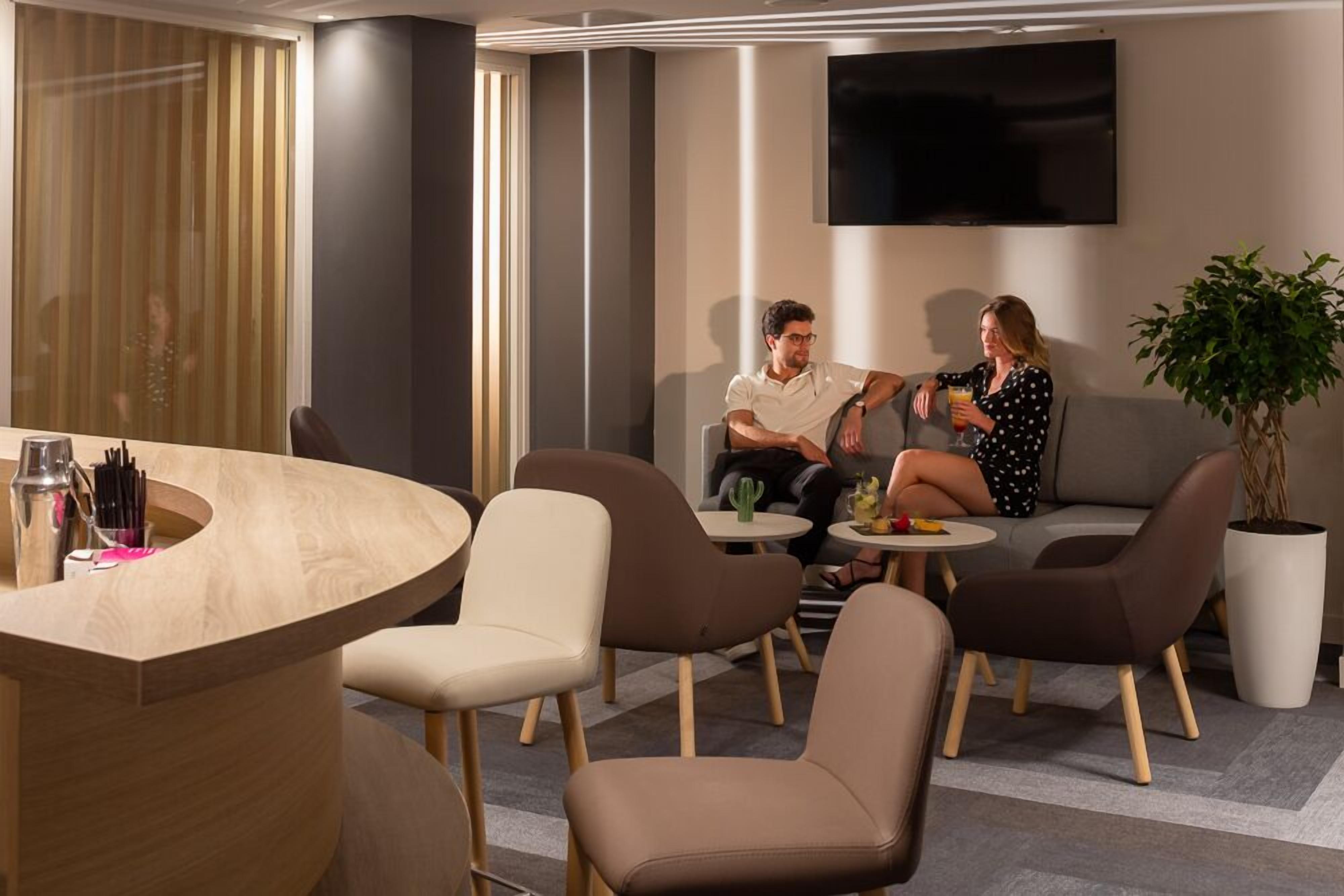A modern lounge area with a curved wooden reception desk, several cushioned seating options, and a large potted plant.