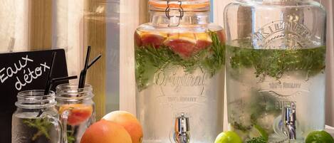Dos grandes frascos de vidrio con grifos metálicos, llenos de agua y diversas frutas y hierbas, junto a frascos más pequeños con pajitas y un letrero que dice "Eaux detox".