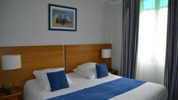 A hotel room with a large bed, two bedside lamps, a framed picture on the wall, and a window with curtains.