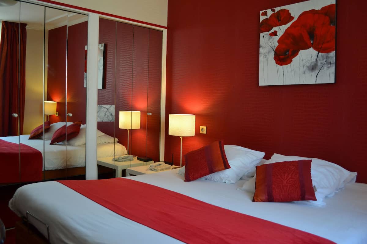 Habitación de hotel con una decoración en rojo y blanco, que incluye dos camas, un espejo, un cuadro de flores rojas y lámparas de noche.