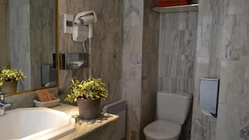 Une salle de bain avec un lavabo en marbre, des toilettes, un sèche-cheveux et une étagère avec une serviette.