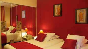 A hotel room with a large bed, red walls, and two framed artworks.