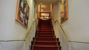 Una imponente escalera con peldaños cubiertos de alfombra roja y barandales dorados, que conduce a un piso superior.