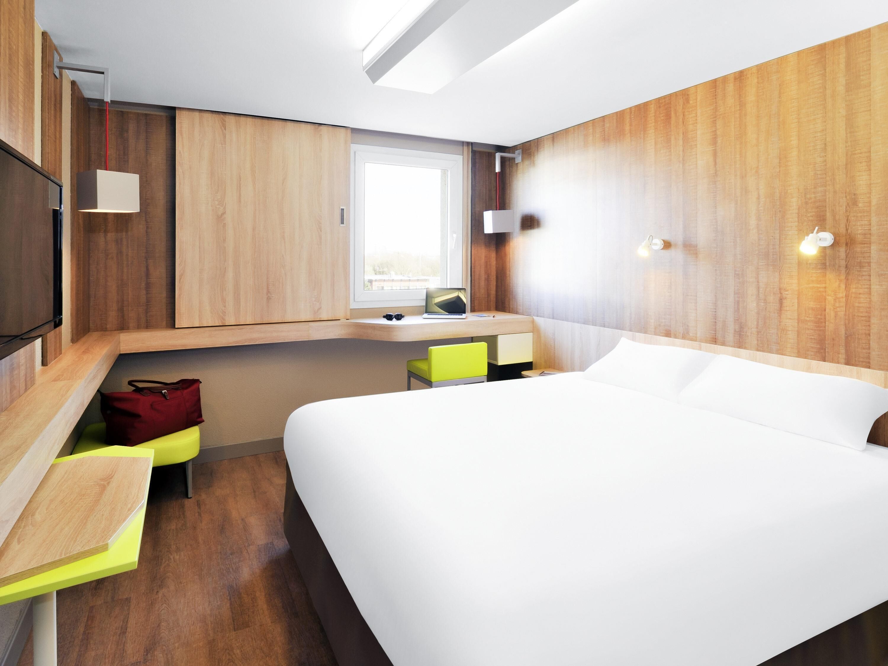 Une chambre d’hôtel moderne équipée d’un lit, d’un bureau, d’une chaise, d’une télévision et d’une fenêtre.