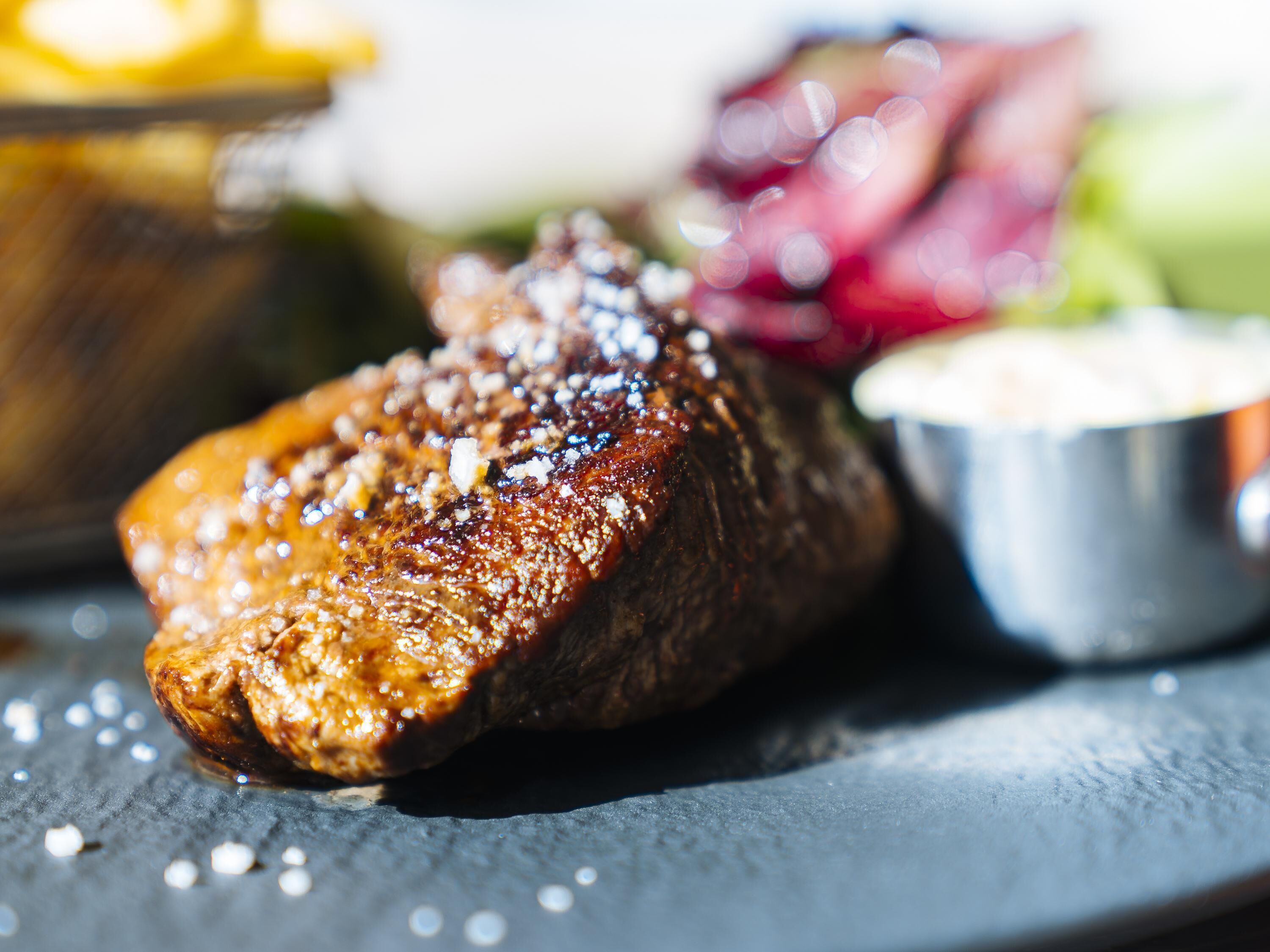 Un steak à la croûte brillante et caramélisée, servi avec une petite portion de sauce et une garniture de légumes marinés.