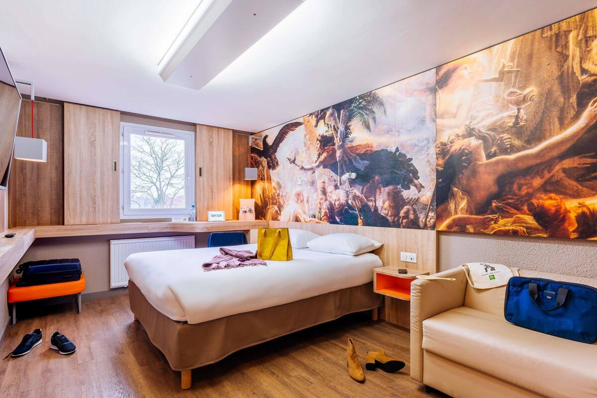 A hotel room with a bed, a sofa, a desk, and a large painting on the wall.