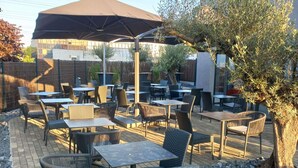 An outdoor patio with tables and chairs, a large umbrella, and a tree. - ibis Styles Lille Marcq en Baroeul (Marcq-en-Baroeul)