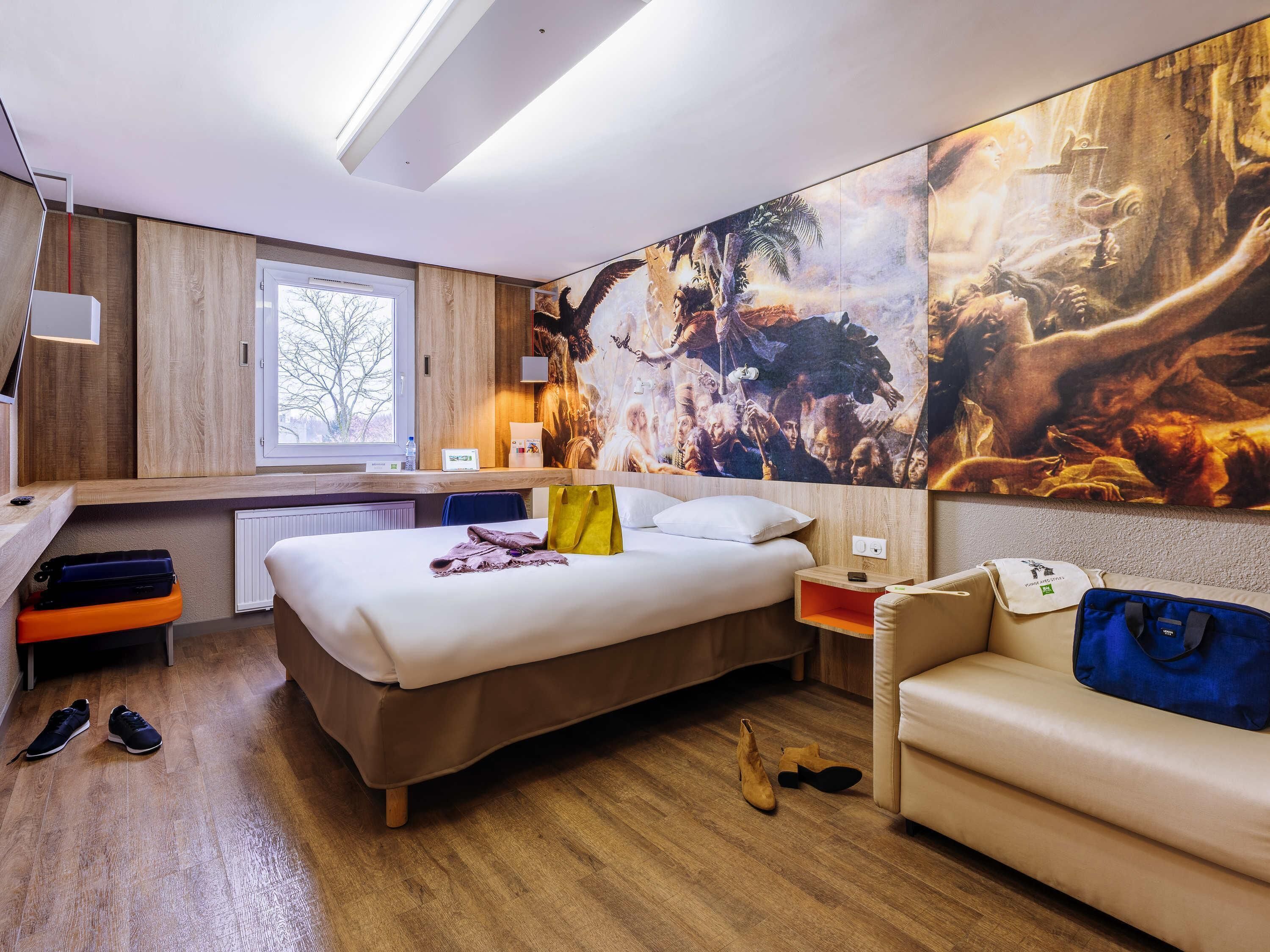 Une chambre d’hôtel avec un lit, un canapé, un bureau, une fenêtre et une grande fresque murale.