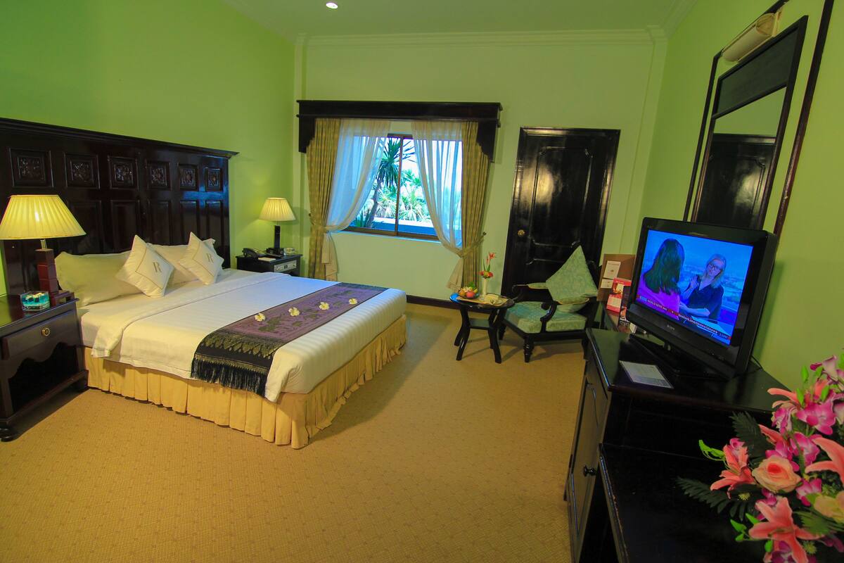 A hotel room with a bed, a television, a desk, a chair, and a window with curtains.