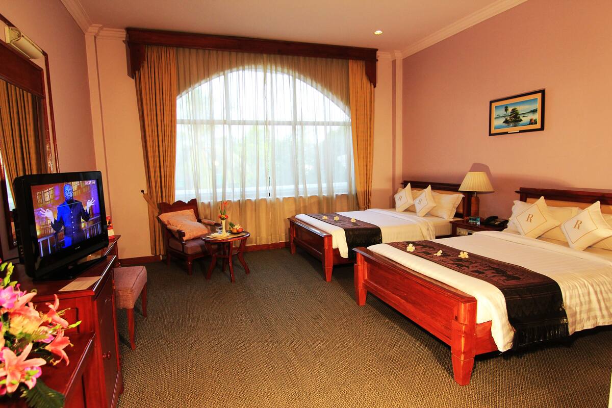 A hotel room with two beds, a television, a desk, and a large window with curtains.