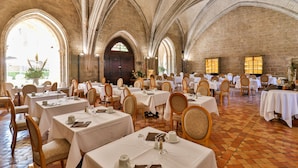 Un salón de banquetes con múltiples mesas dispuestas para comer, techos abovedados y grandes ventanales que permiten la entrada de luz natural.