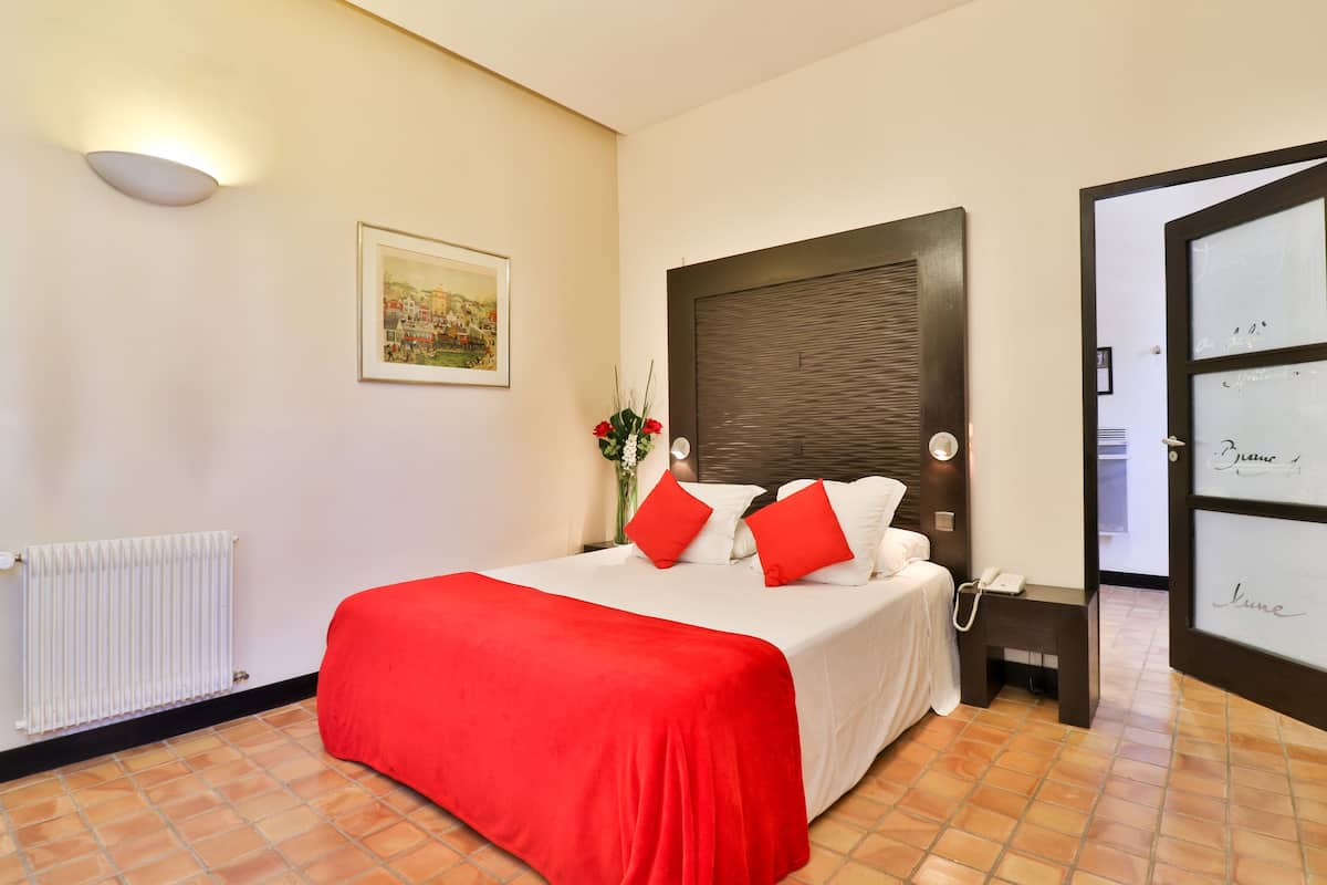 Un dormitorio ordenado con cama, mesita de noche, radiador y puerta con panel de vidrio esmerilado.