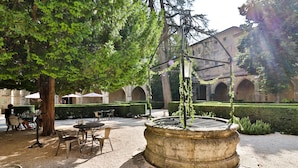 Un patio al aire libre con una fuente, zona de estar y un edificio con arcos al fondo.
