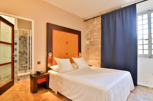 Habitación de hotel con cama, mesita de noche, teléfono, zona de ducha y vista al exterior.