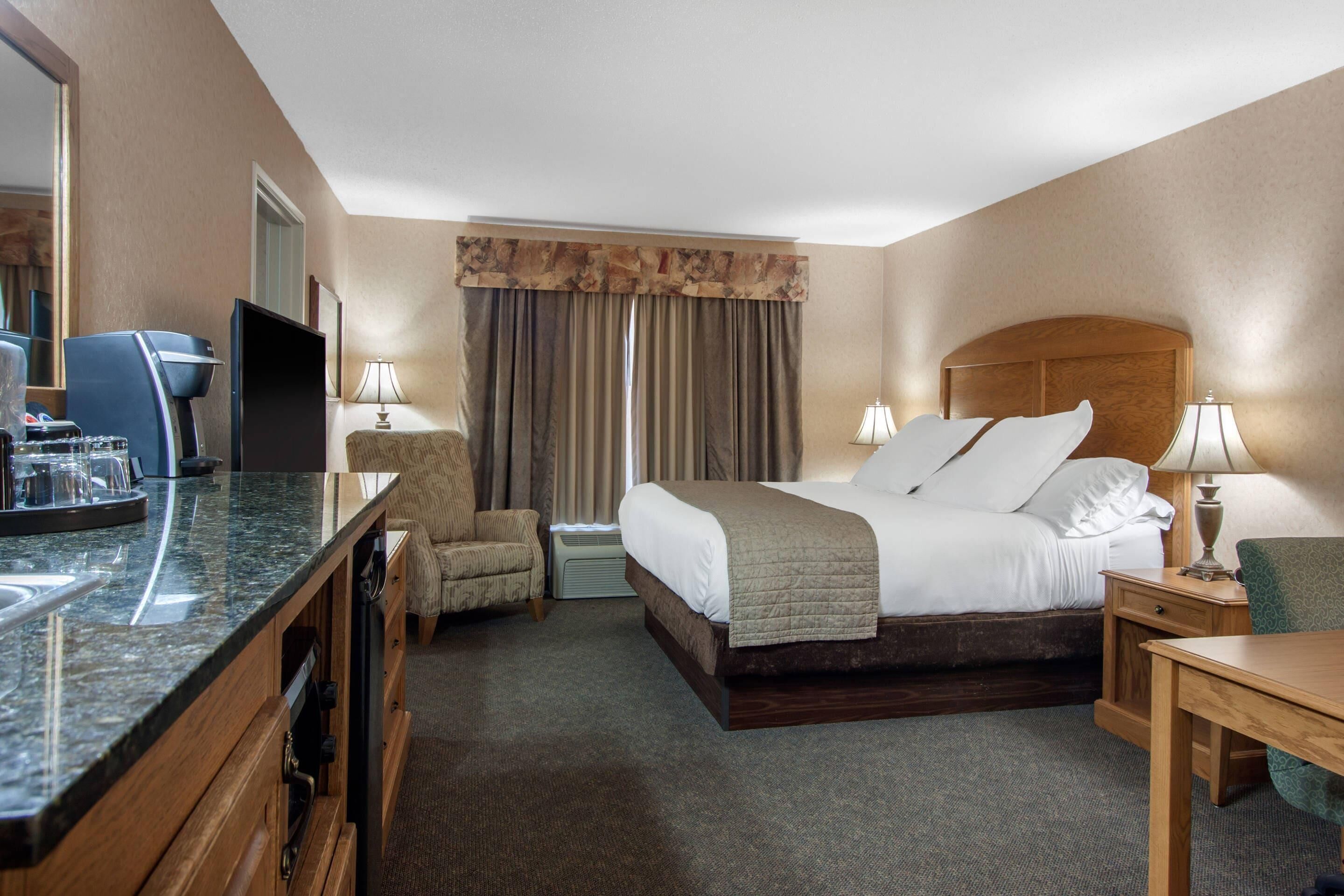 A hotel room with a bed, a desk, a chair, a TV, and a minibar.