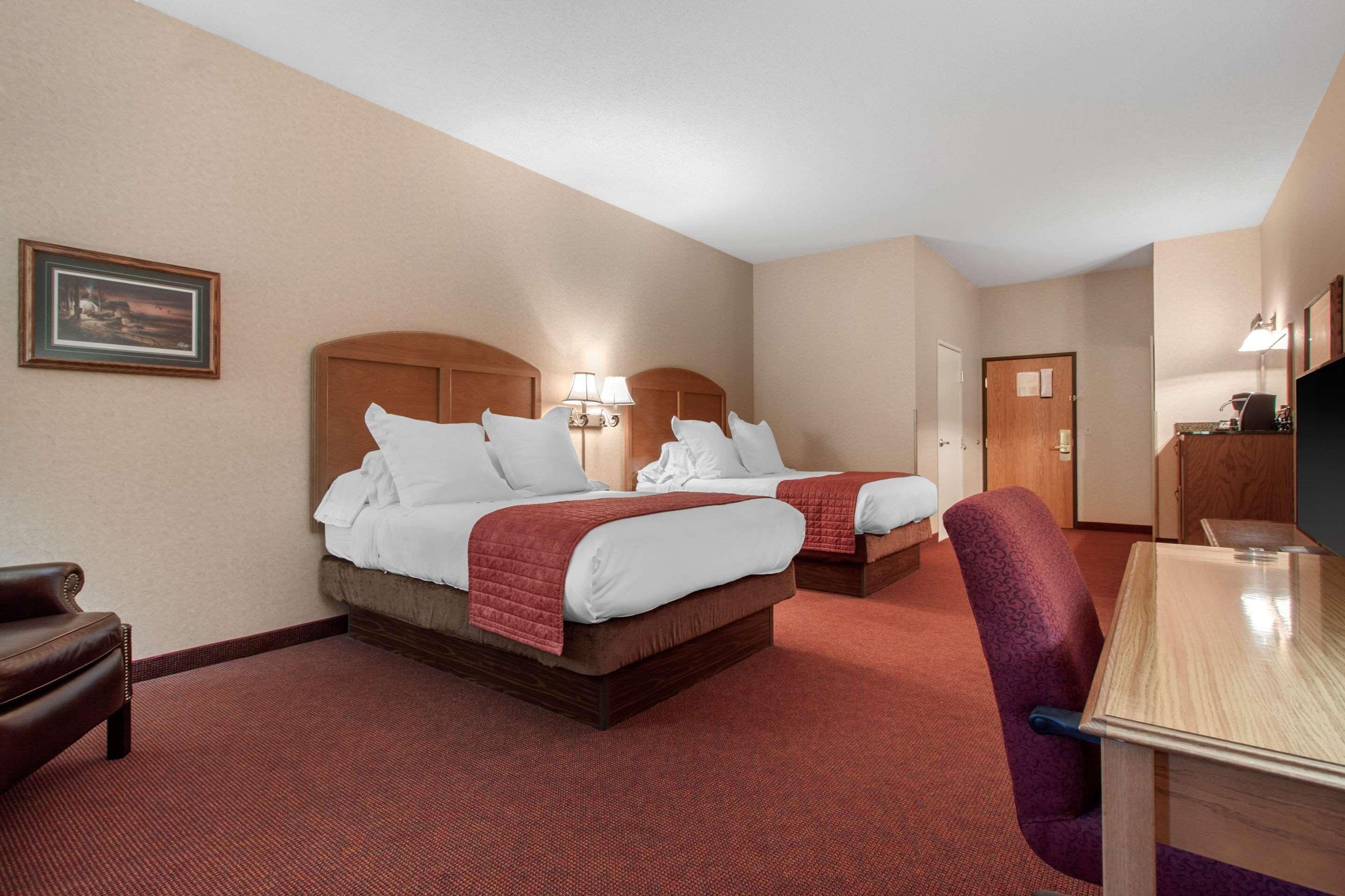 A hotel room with two beds, a desk, a chair, and a television.
