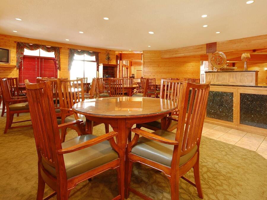 Un comedor de madera con una mesa redonda y sillas, una cocina al fondo, y un televisor montado en la pared.