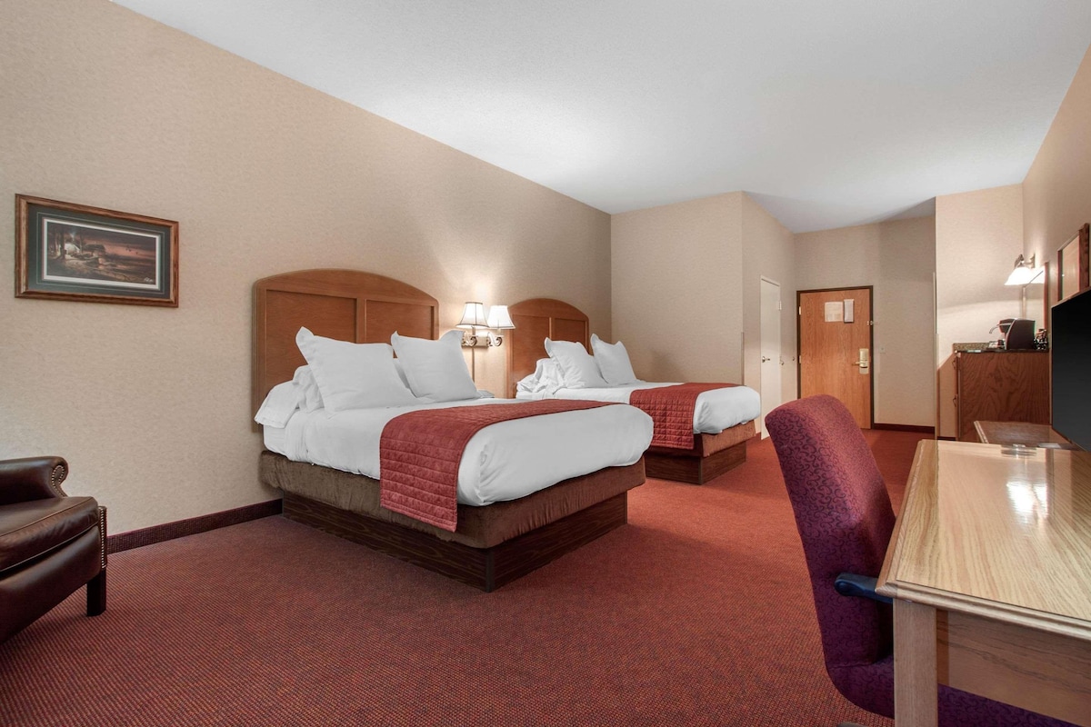 A hotel room with two beds, a desk, a chair, and a television.