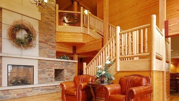 A wooden interior with a fireplace, leather chairs, a wooden staircase, and a chandelier. - Norfolk Lodge & Suites, an Ascend Collection Hotel (Norfolk)