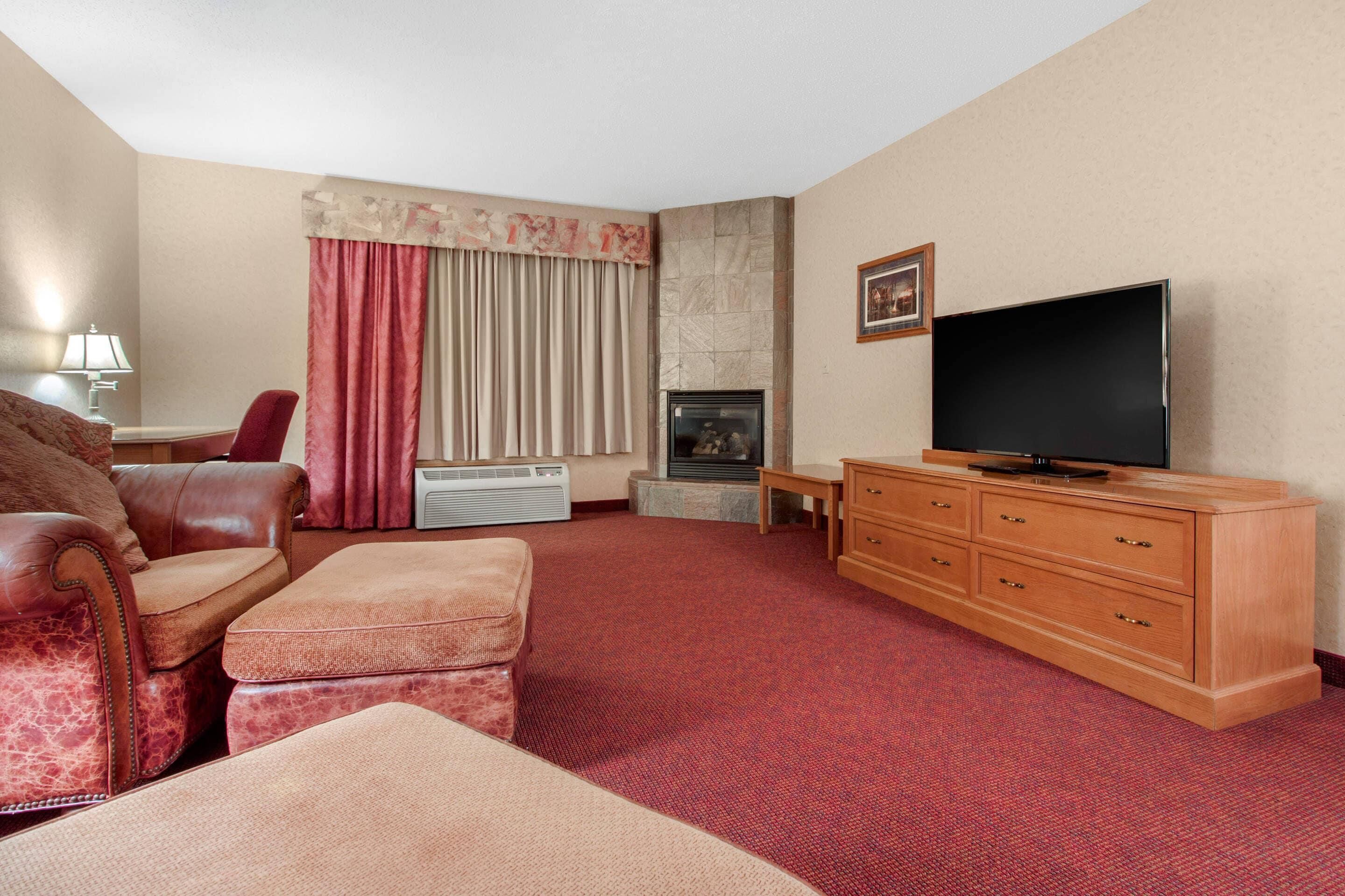 Ett hotellrum med en röd matta, en soffa i läder, ett TV-bord i trä och en öppen spis.