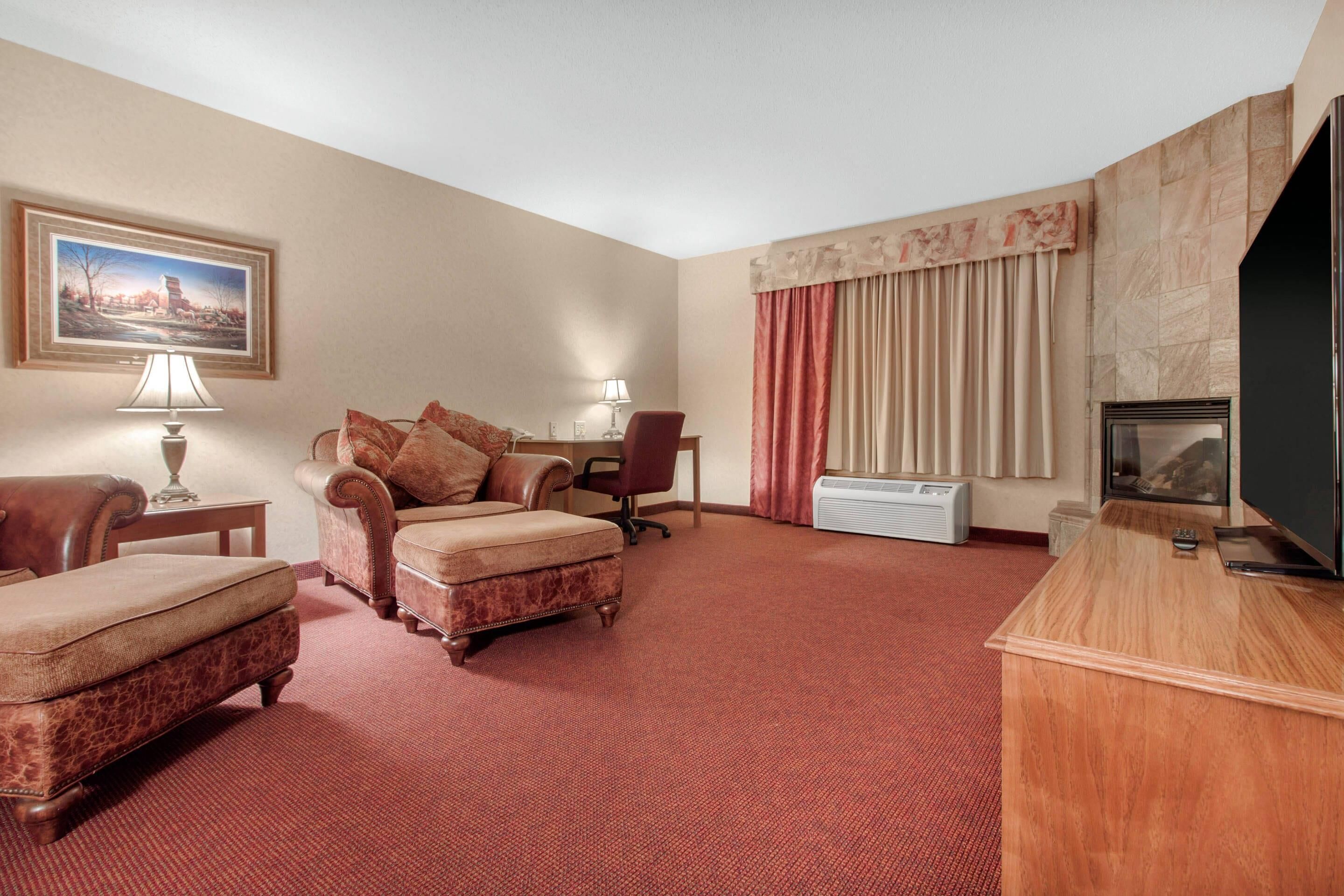 A hotel room with a sofa, ottoman, chair, TV, and a painting on the wall.