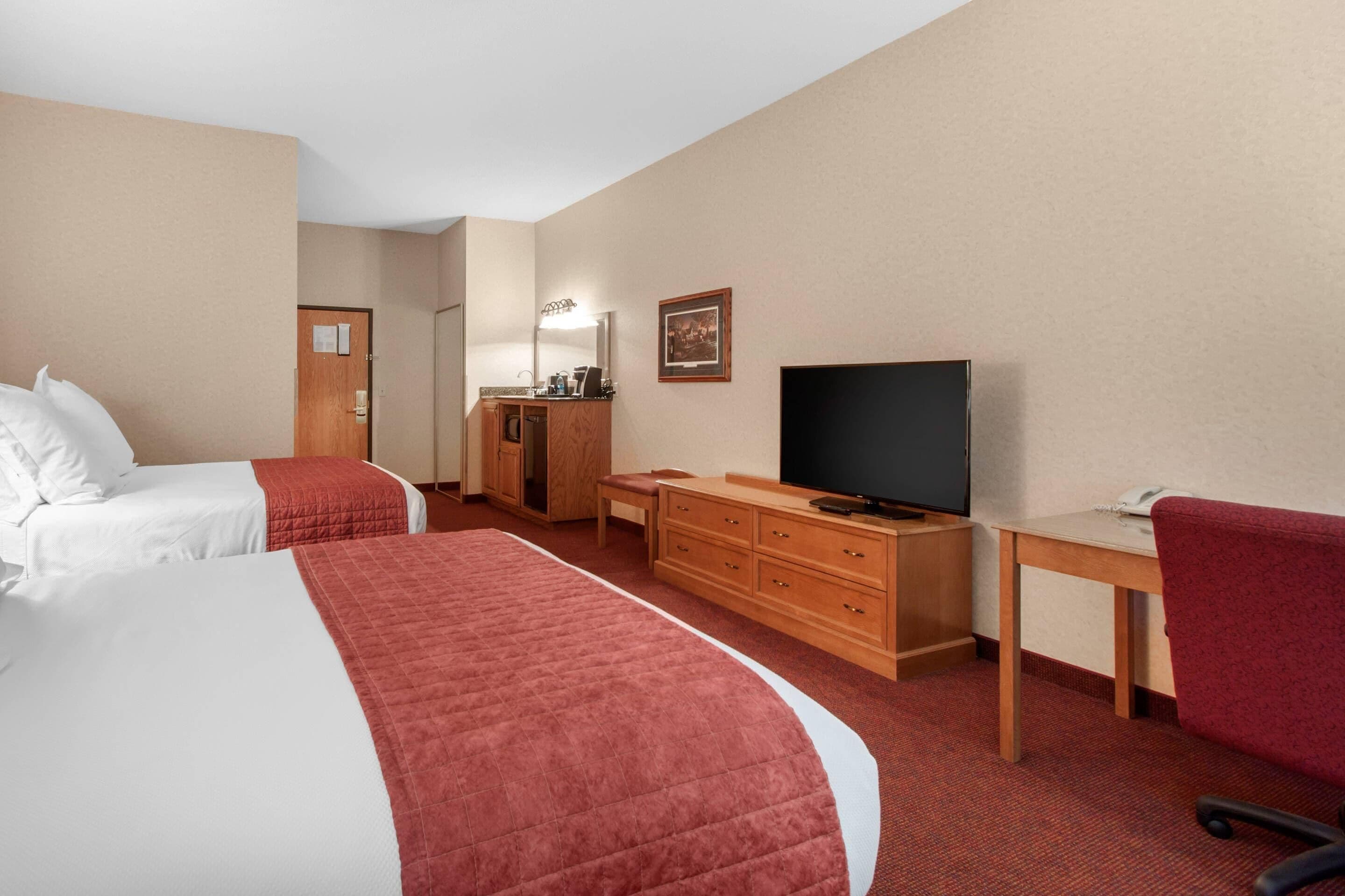 A hotel room with two beds, a TV, a desk, and a chair.