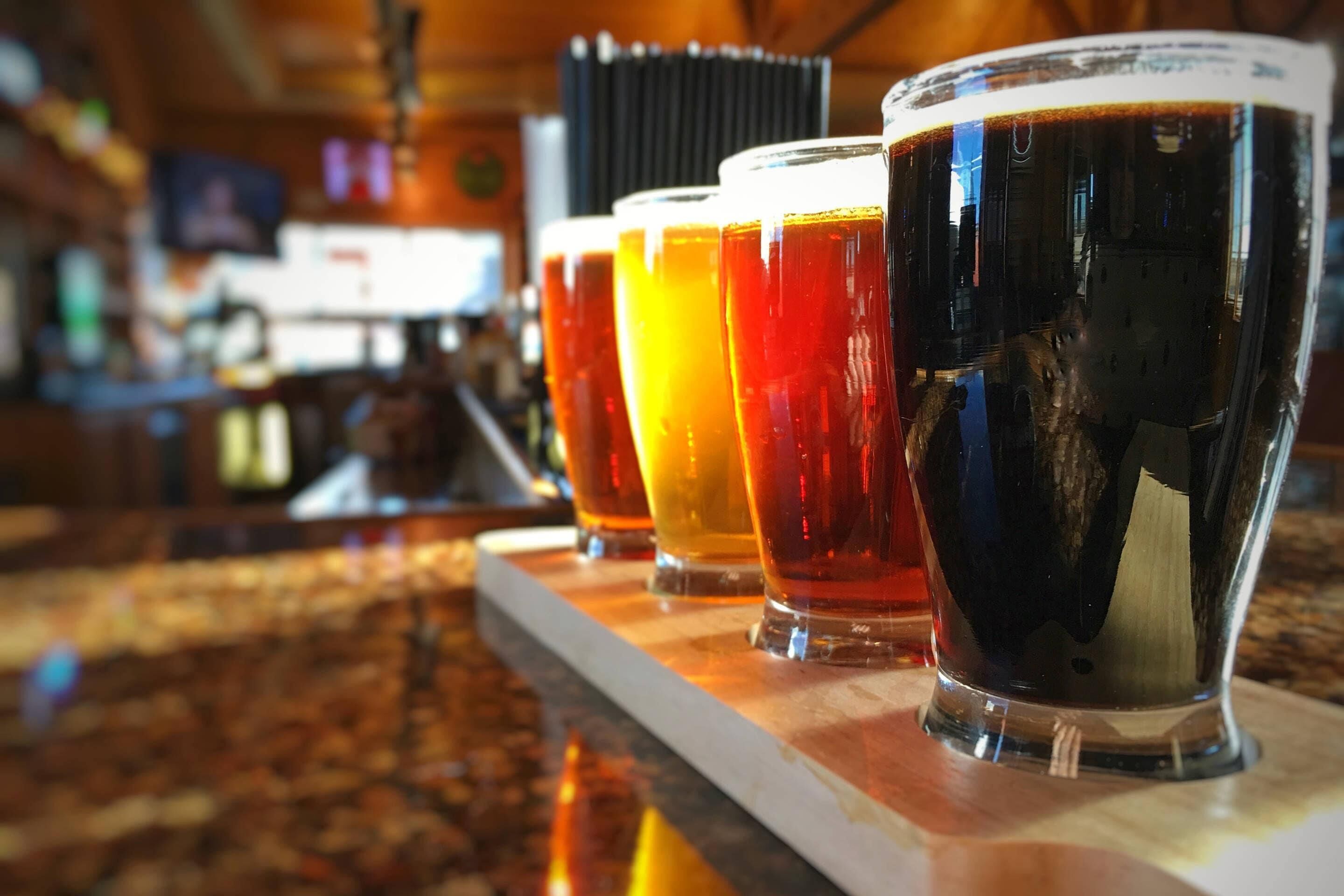 A row of glasses with different colored beverages on a bar counter.