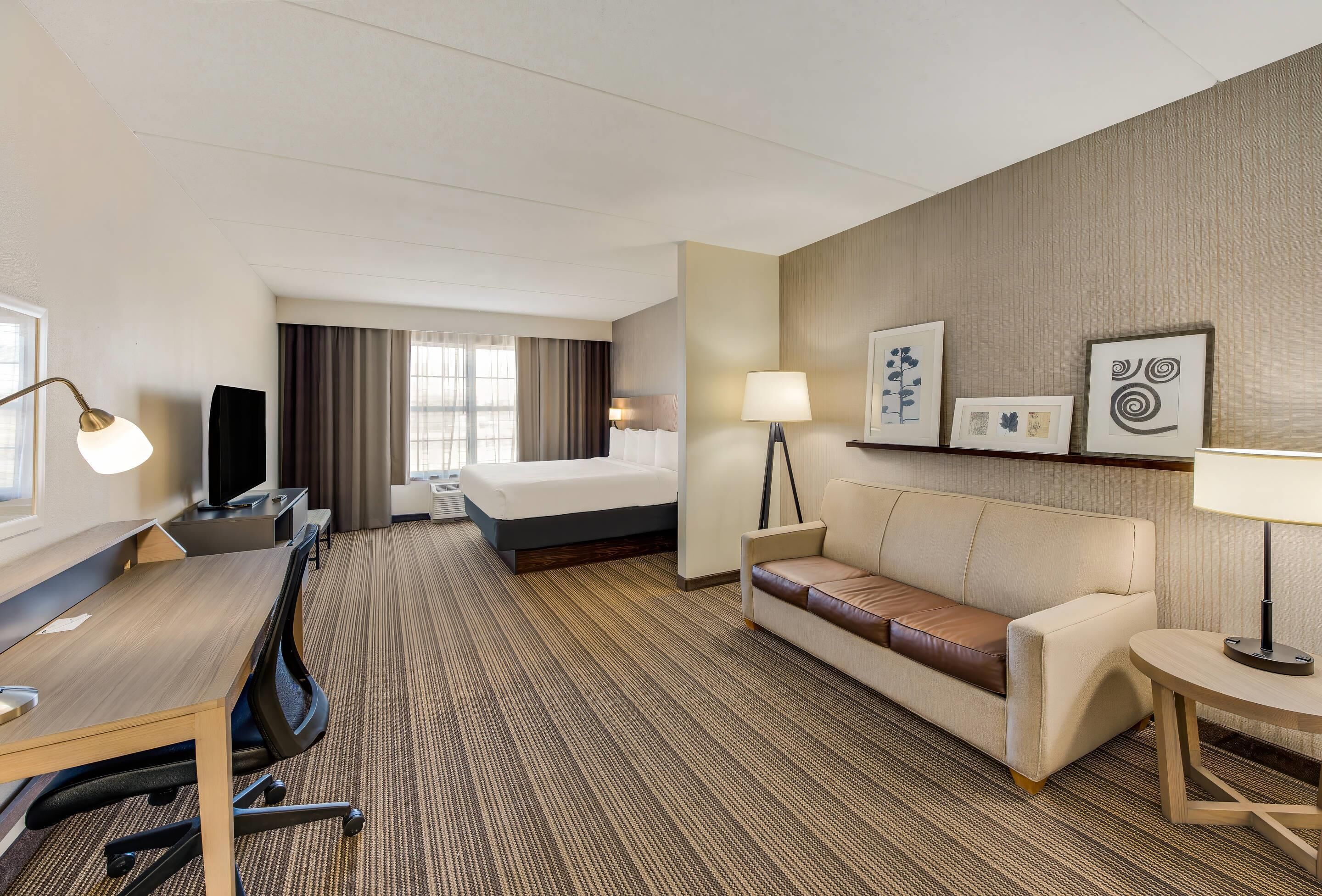 Quarto de hotel com cama, sofá, escrivaninha com cadeira, televisão e quadros na parede.