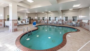 Une piscine intérieure au design incurvé, entourée de chaises longues et dotée d’un sol carrelé.