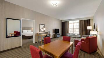 A hotel room with a bed, desk, TV, and seating area.