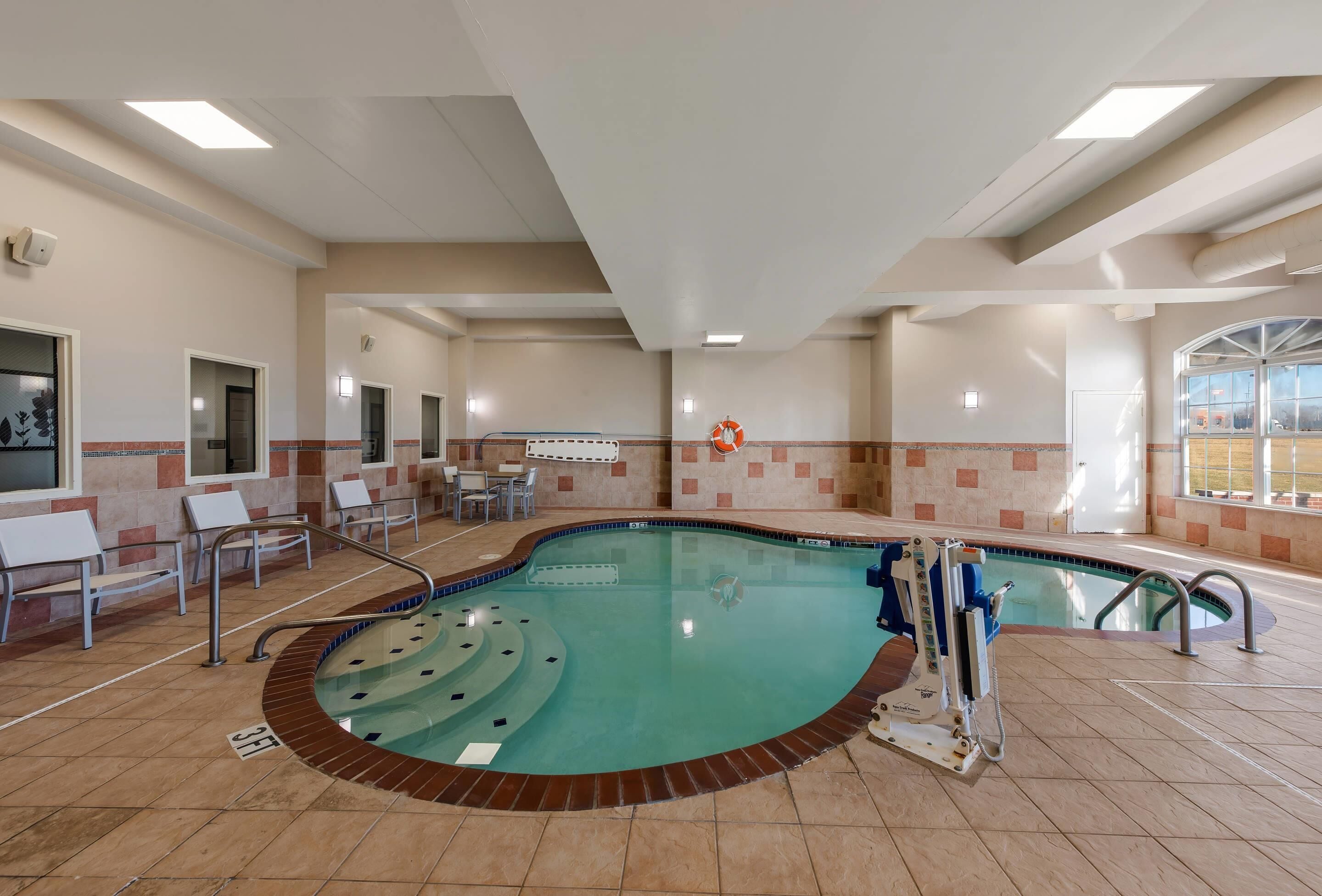 An indoor swimming pool with a lifeguard chair, lounge chairs, and a sunroof.