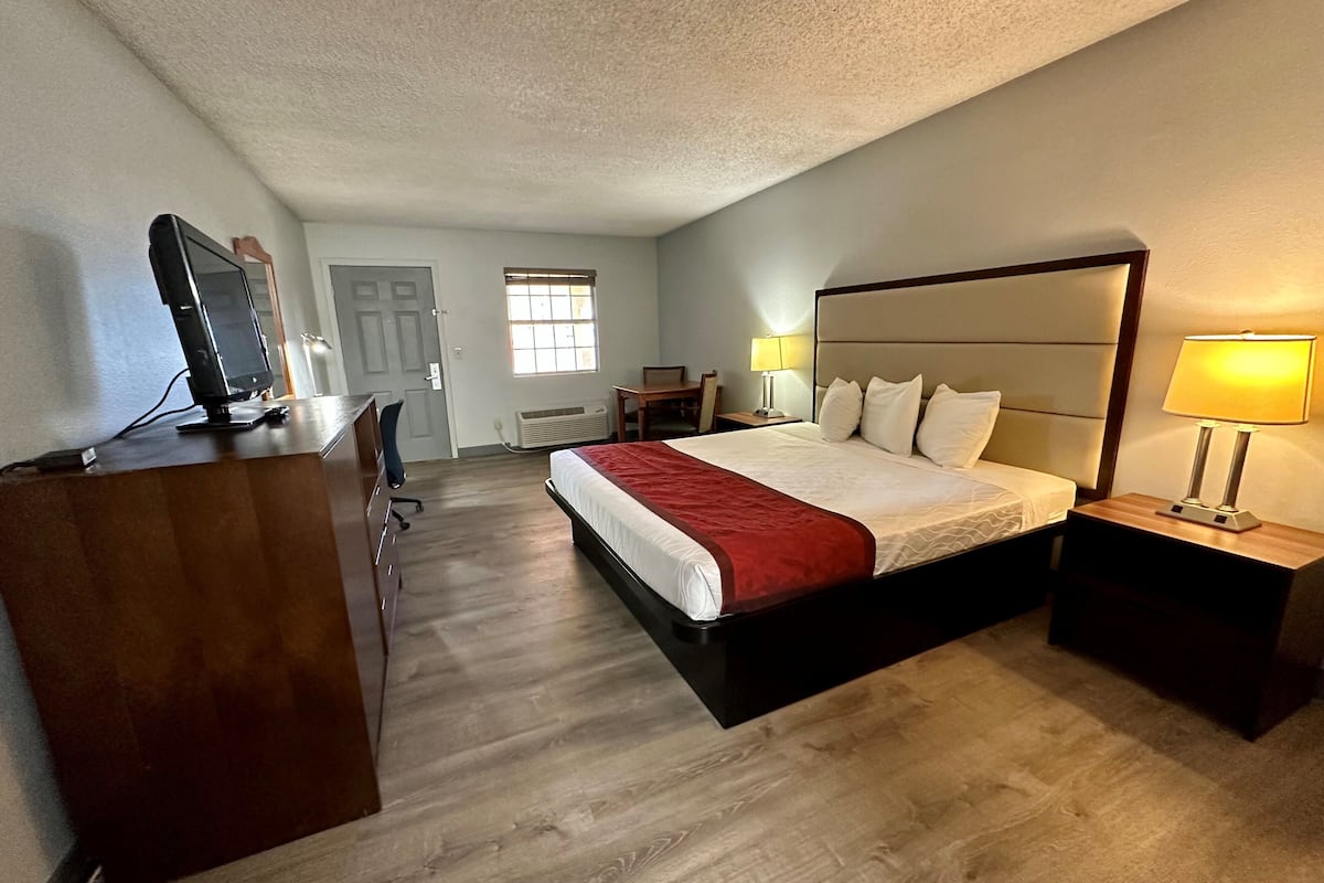 A hotel room with a large bed, bedside lamps, a desk with a computer, and a chair.