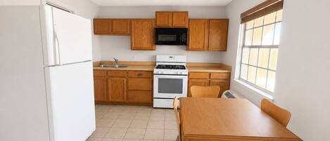 A kitchen with wooden cabinets, a white refrigerator, a microwave, an oven, and a dining table with chairs.